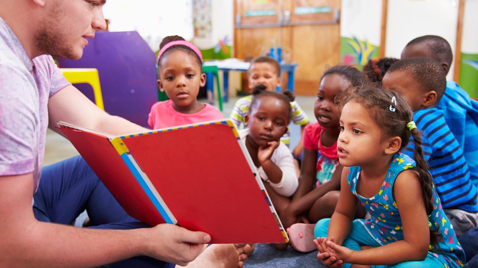 Volunteer teacher reading to a class of preschool kids stock photo